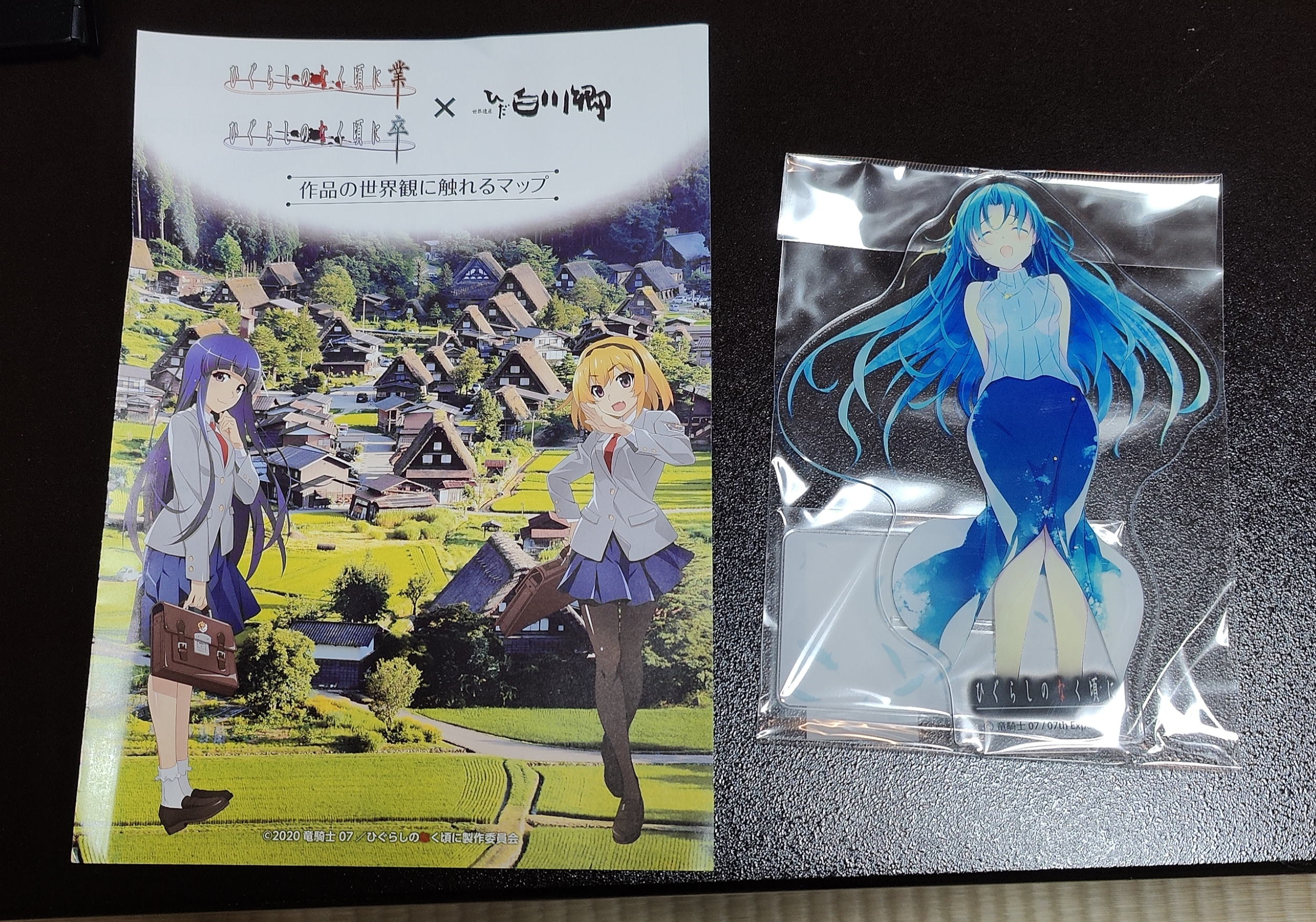 The front page of the map I was given and Shion standee I purchased. The map was printed in 2020 and features art of Rika and Satoko standing over a shot of the village. It is adorned with the official logos of the newest Higurashi anime and the Shirakawa-go tourist board