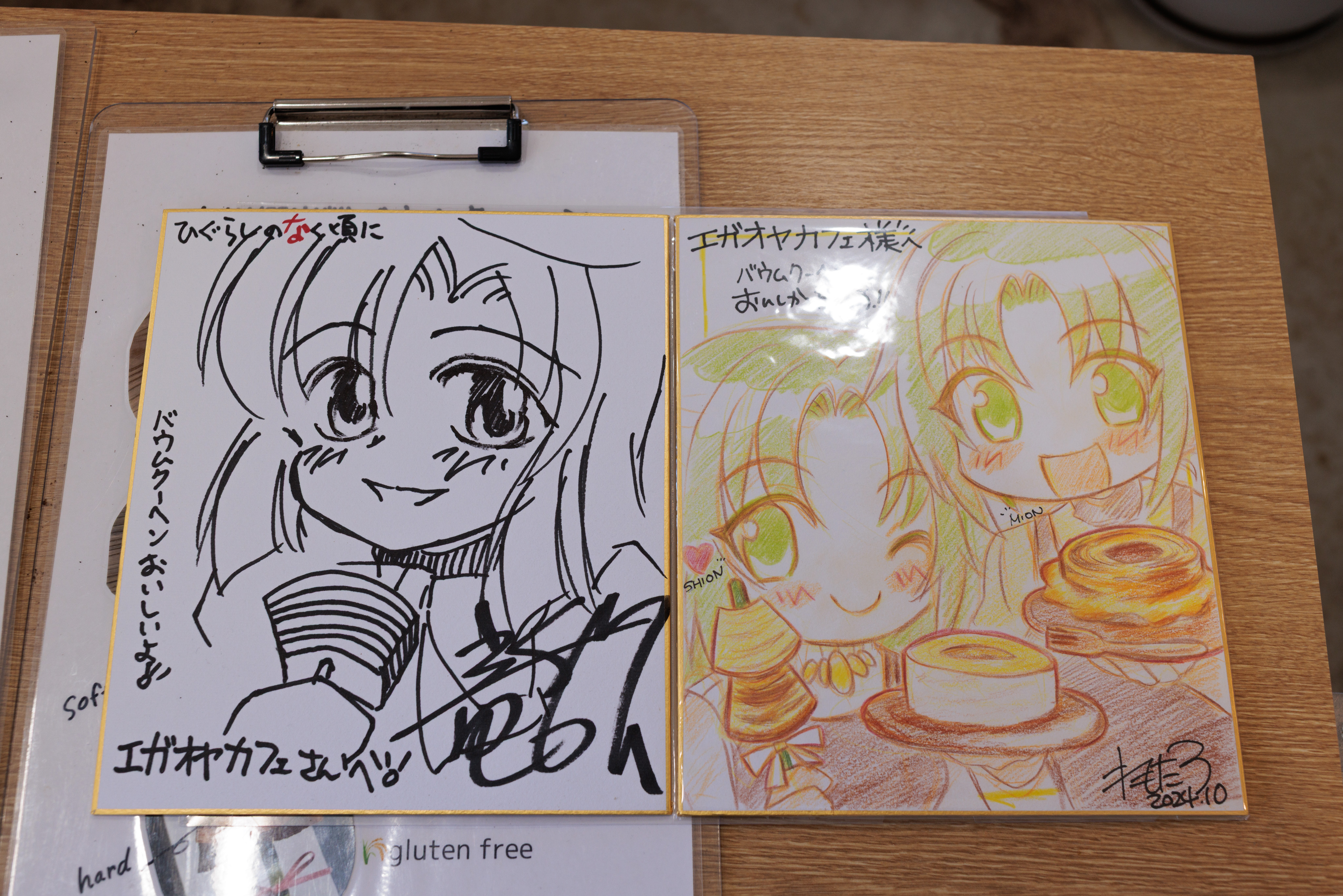 The shikishi drawn by Ryukishi07 and Remotaro. The Ryukishi one features Rena holding some baumkuchen on a stick, whereas the Remotaro art shows the Mion and Shion with the same.